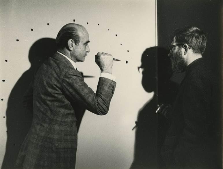 “Eski resim formüllerini, geleneksel sanat görüşünü arkamda bırakmak için tuvalde bir delik açıyorum ve hem sembolik anlamda hem de somut olarak, durağan yüzeyin zindanından kaçıyorum” diyen Lucio Fontana (1899-1968) ile Belçikalı sanatçı Jef Verheyen (1932-1984), 1962 yılında tuhaf bir mekanda bulunuyorlar. Fontana elindeki aletle Verheyen’in tuvalinin üstüne delikler açıyor. İşini yaklaşık 10 saniyede bitiriyor. Bu bir sanat eserinin yapılış, meydana geliş sürecini gösteriyor. Sanatçıya göre iş, tuvalde kalan izler değil, tuvale bu izlerin yapıldığı süreç. Fotoğraf:news.artnet.com